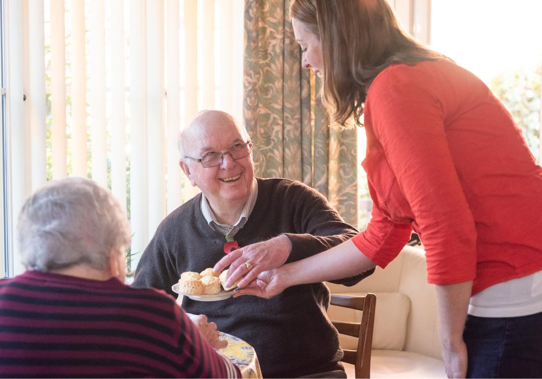 Care companion serving scones to a couple at home